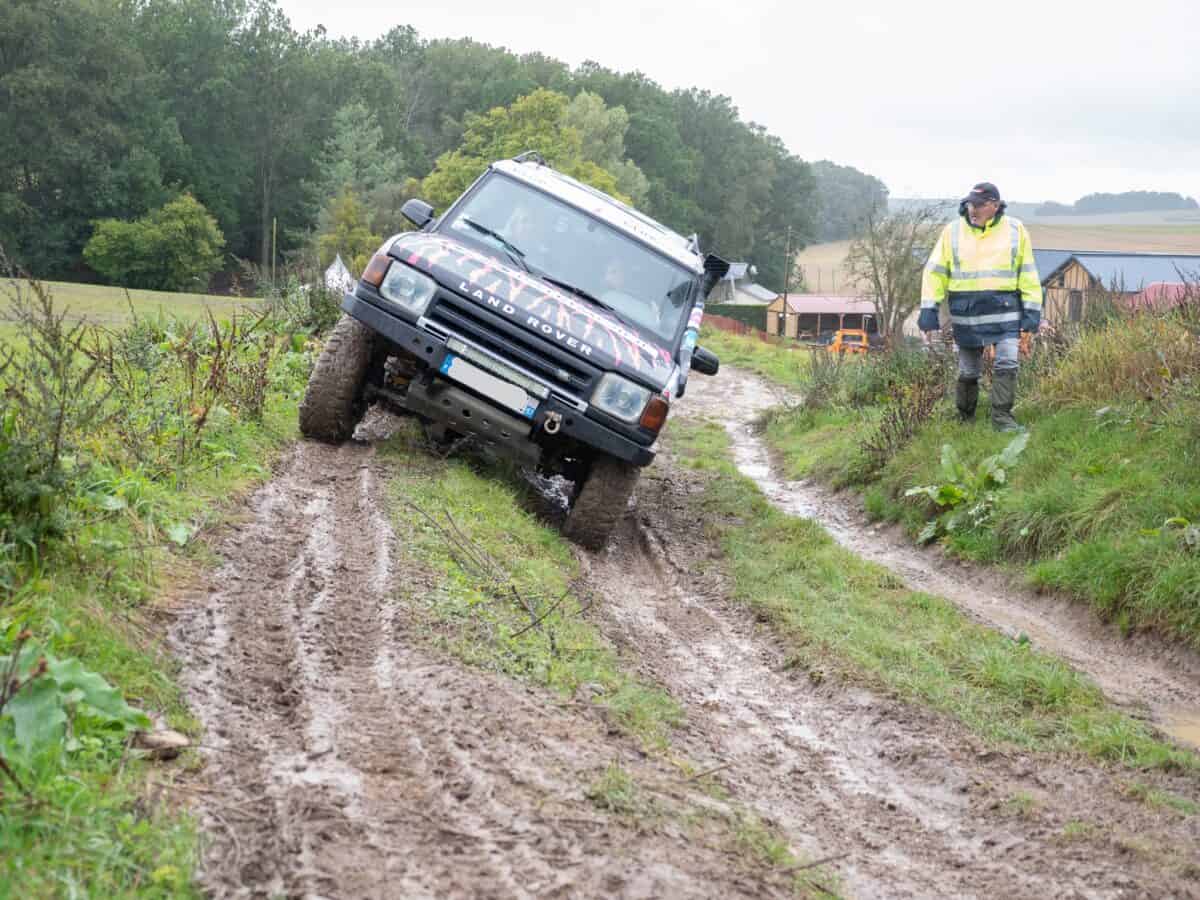 formateur en pilotage 4x4 marchant à côté d'un 4x4 qui circule sur un chemin boueux lors d'un exercice pratique